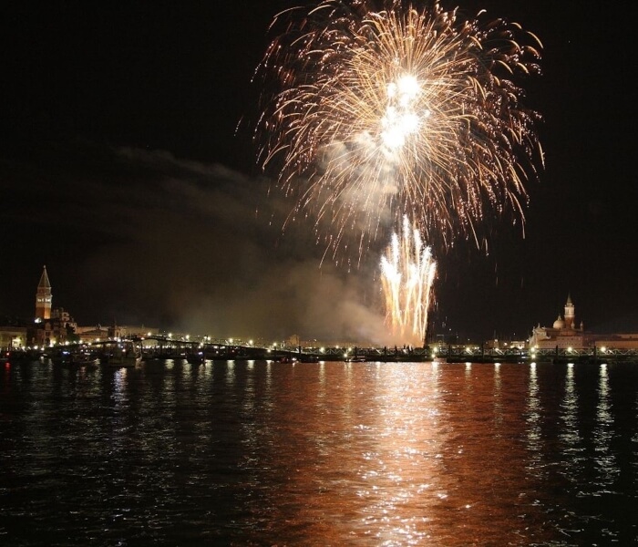 Fuochi d'artificio brillano sopra l'acqua con riflessi luminosi.