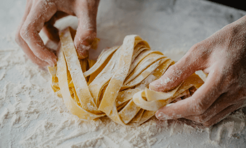 Mani spolverano una pila di fettuccine fresche con farina.