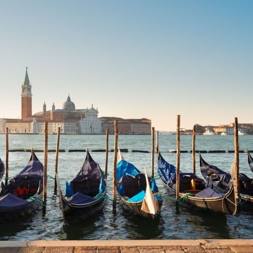 Gondole ormeggiate a Venezia, con skyline e cielo sereno, trasmettono un'atmosfera di tranquillità.