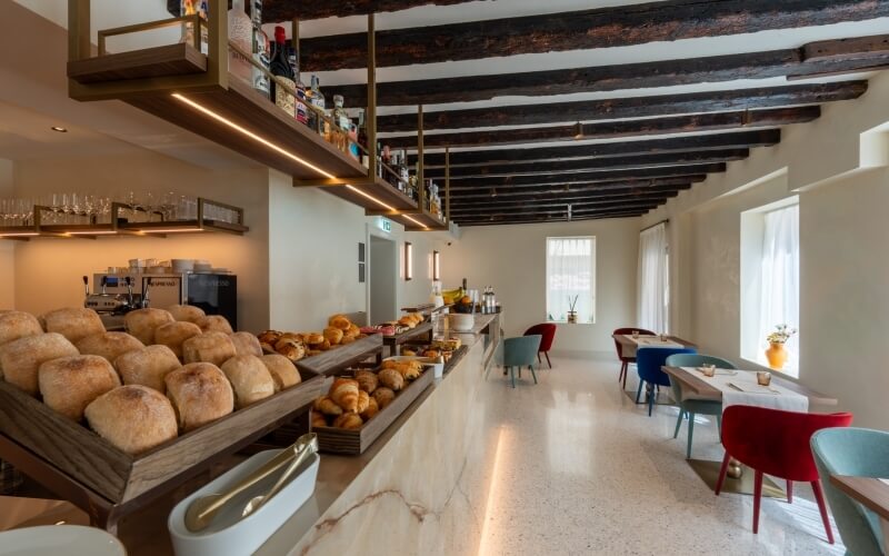 Colazione a buffet con pane, dolci e tavoli sullo sfondo.