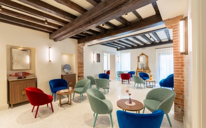 Area di sosta con sedie colorate e tavoli, soffitto in legno.