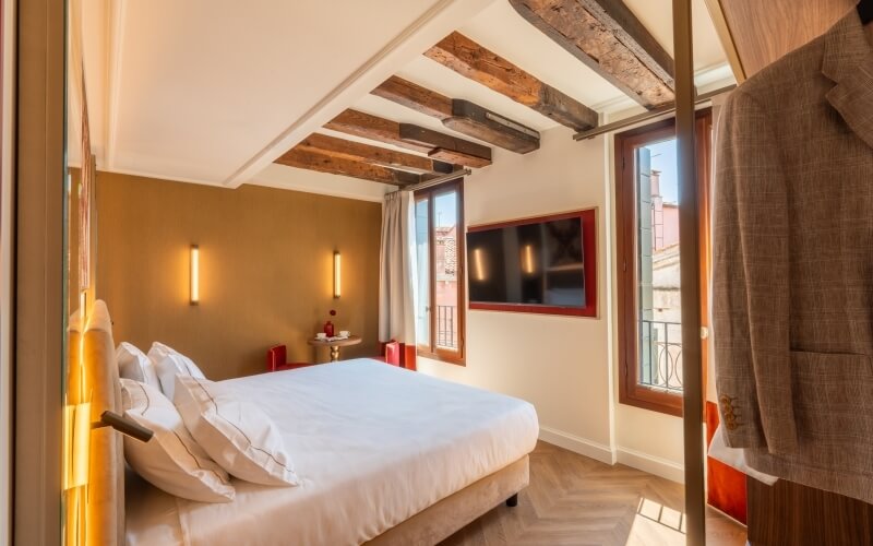 Hotelzimmer mit Bett, TV, Holzdeckenbalken und Fensterblick.