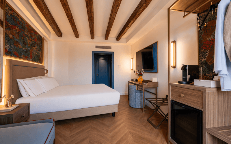 Camera d'hotel con letto, scrivania, TV e soffitto in legno.