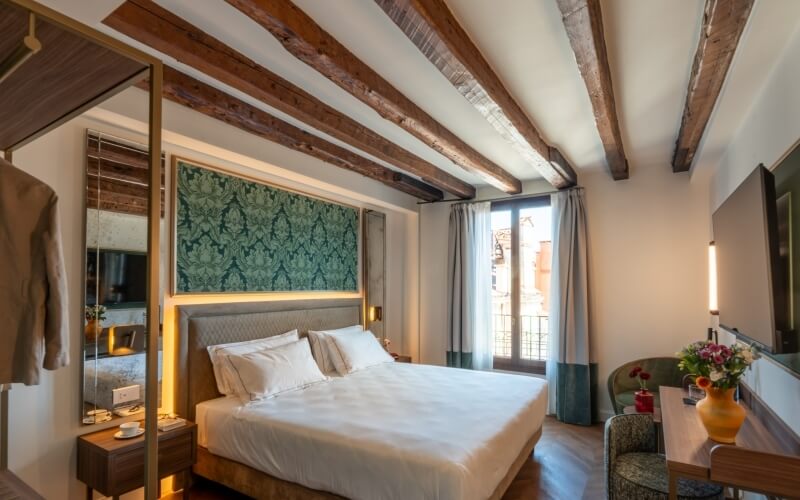 Hotelzimmer mit Bett, Nachttisch, Schreibtisch und Balkonfenster.