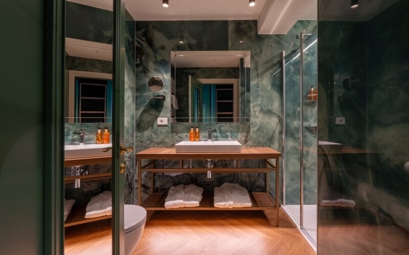 Bagno d'hotel con lavabo in legno, doccia in vetro e marmo verde.