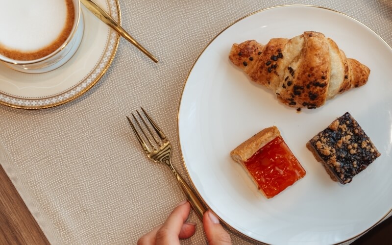 Piatto bianco con croissant e dolci, tazza con bevanda schiumosa.