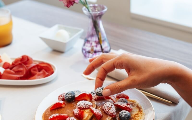 Persona aggiunge mirtilli a pancake con fragole e zucchero a velo.