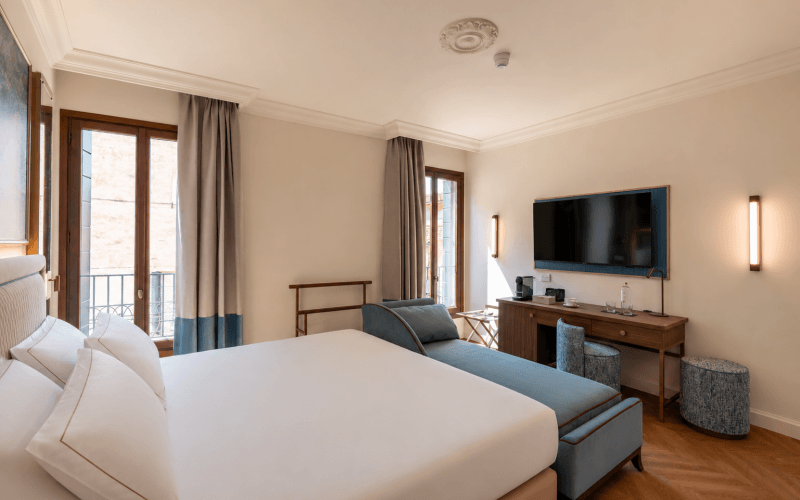 Camera d'hotel con letto grande, balcone e chaise lounge blu.
