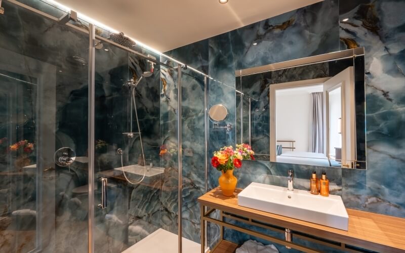 Badezimmer mit Glasdusche, Holzwaschtisch und buntem Blumenstrauß.