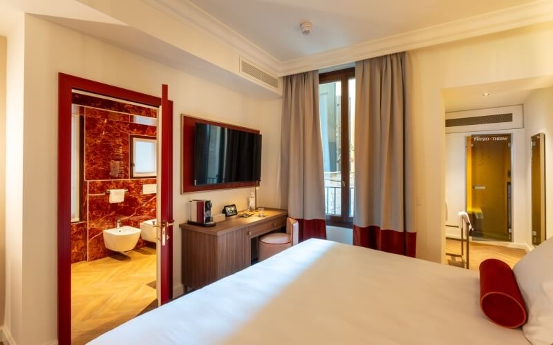 Camera d'hotel con letto, scrivania e bagno in marmo rosso.