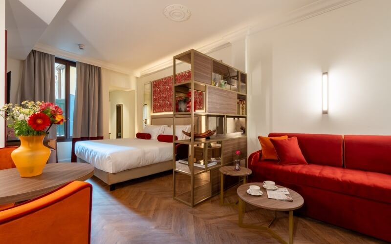 Camera d'hotel con letto, divano rosso e scaffale moderno.