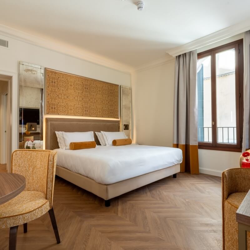 Camera d'hotel con letto grande, sedie e finestre con balcone.