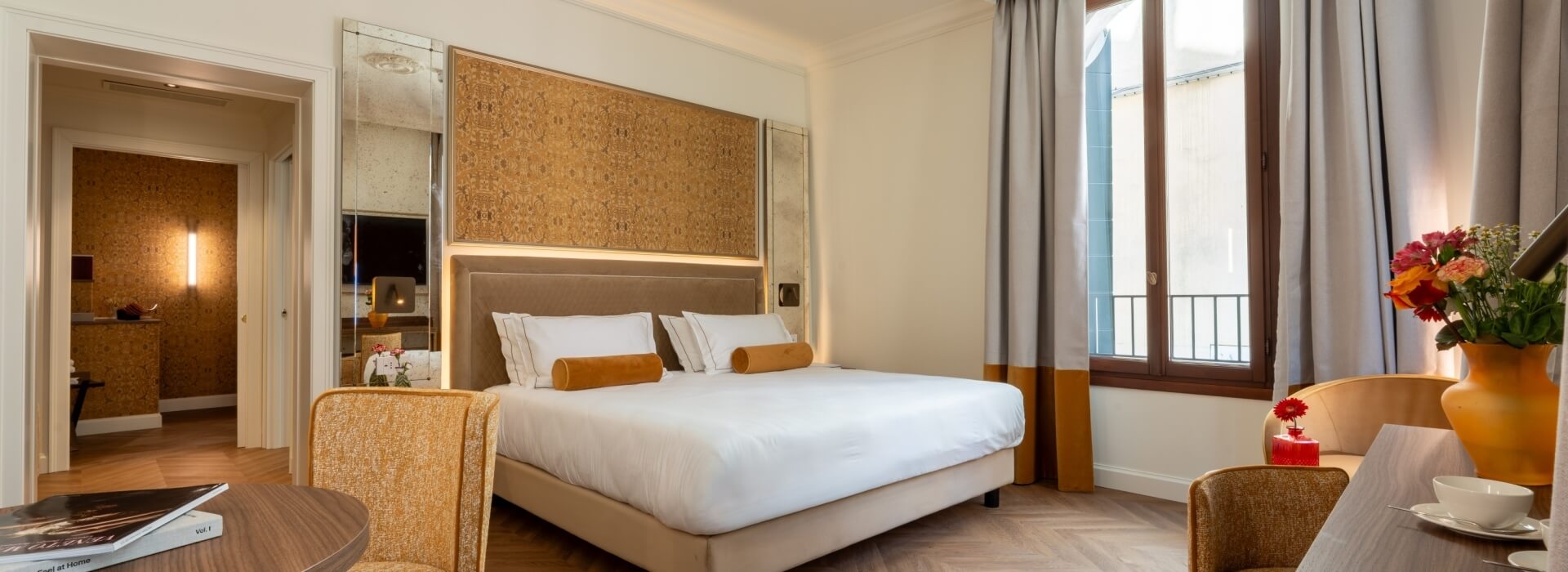 Hotel room with bed, mirrors, balcony, and flower vase.