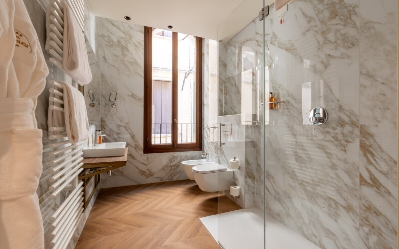 Bagno moderno con accappatoi, lavabo, doccia in vetro e pavimento in legno.