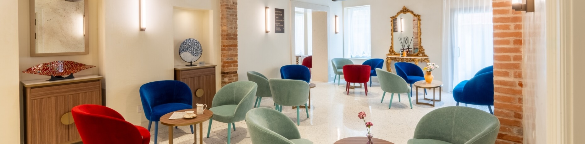 Lobby con sedie colorate, tavolini e specchio dorato.