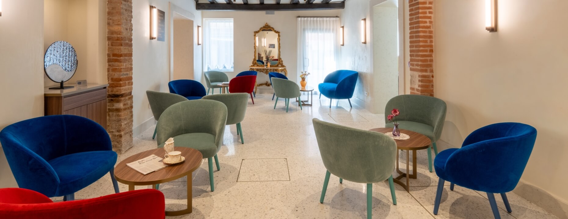 Hotel lounge with colorful armchairs, round tables, and ornate mirror.