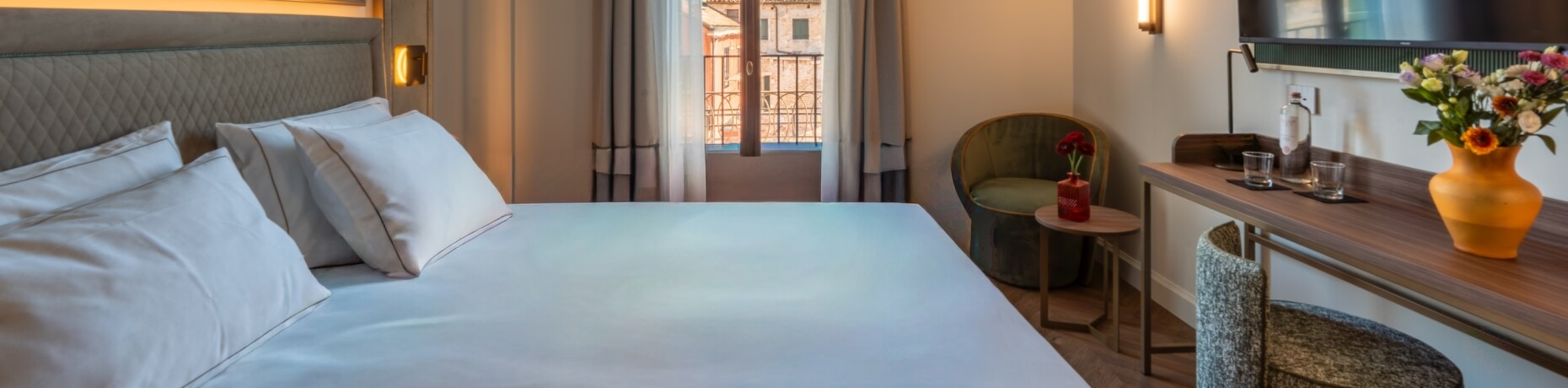 Camera d'hotel con letto, scrivania e fiori decorativi.