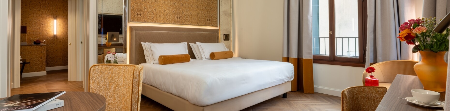 Hotelzimmer mit Bett, Stühlen, Tisch und Fenster mit Vorhängen.