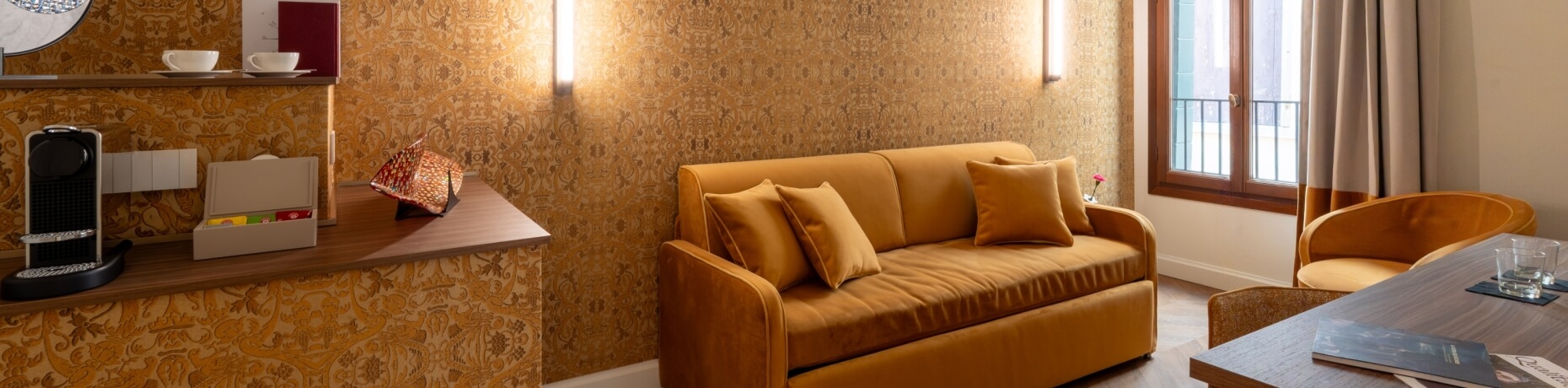Hotelzimmer mit Couch, Sessel, Tisch, Fenster und Kaffeemaschine.