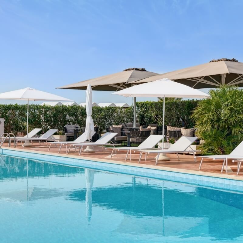 Piscina con lettini e ombrelloni, cielo sereno e chiaro.