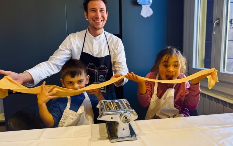 Uomo e bambini tengono una lunga sfoglia di pasta gialla.