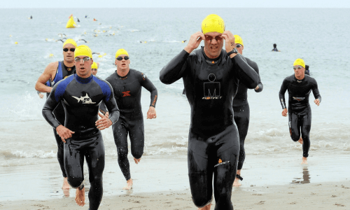 Gruppo di atleti in muta corre sulla spiaggia dopo il nuoto.