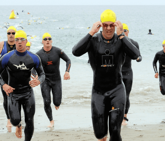 Nuotatori in mute nere e cuffie gialle corrono verso il mare.