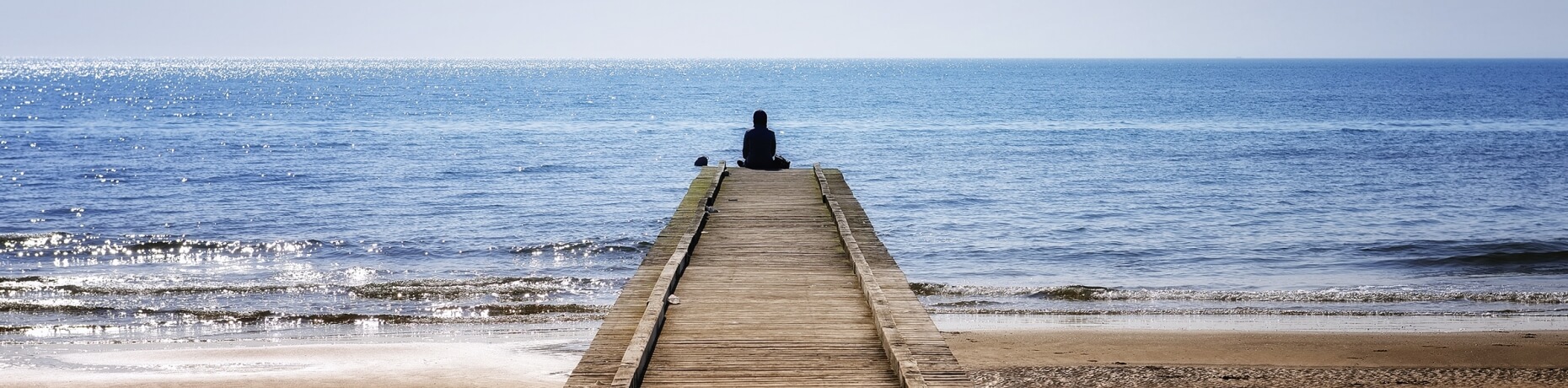 Un molo di legno si estende nel mare blu, con una persona seduta.