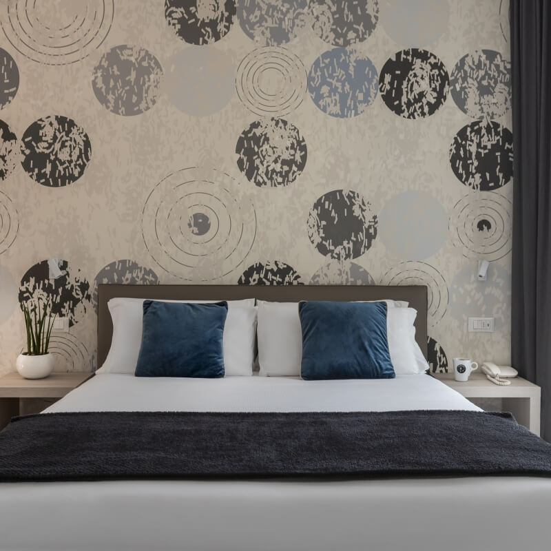Camera d'hotel con letto bianco, cuscini blu e decorazioni grigie.