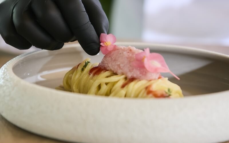 Mano guantata nera aggiunge un fiore rosa a un piatto di pasta.