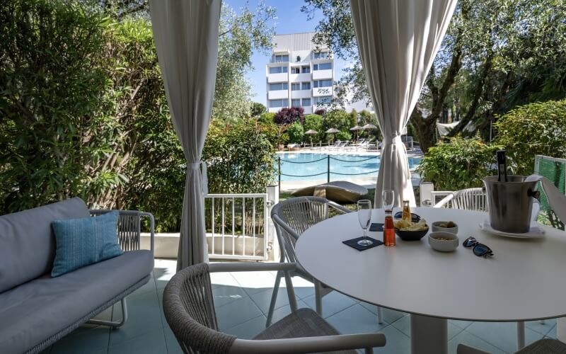 Ein ruhiger Außenbereich mit Patio, Pool, Tisch mit Wein und Snacks, umgeben von üppigem Grün und einem großen Gebäude.