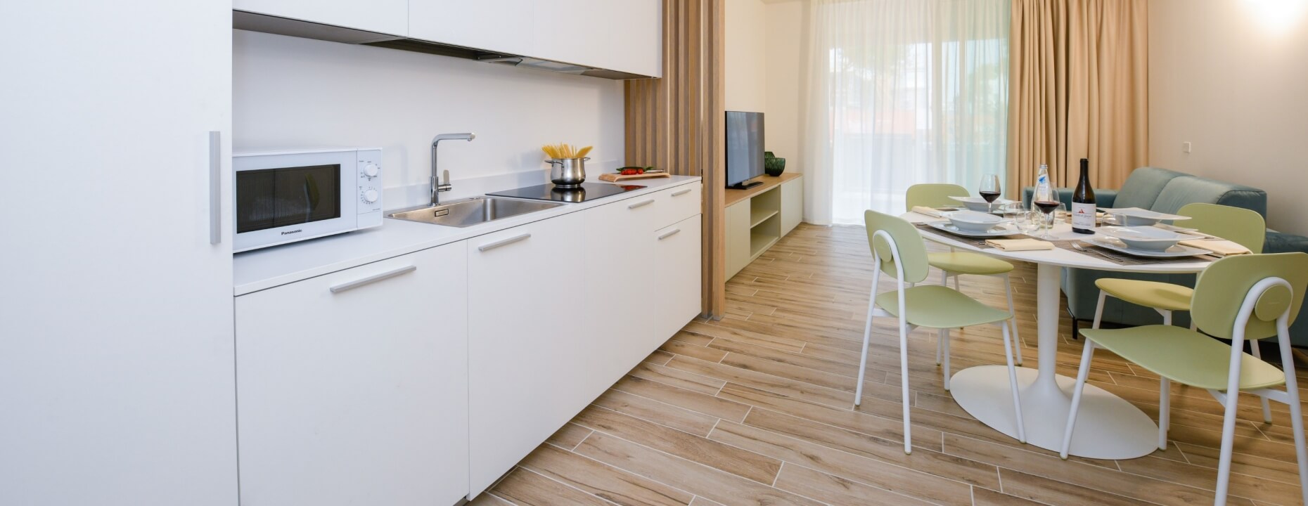 Cucina con mobili bianchi, tavolo da pranzo e divano sullo sfondo.