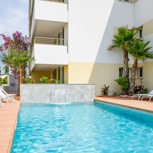 Piscina con acqua blu, parete con cascata e palme circostanti.