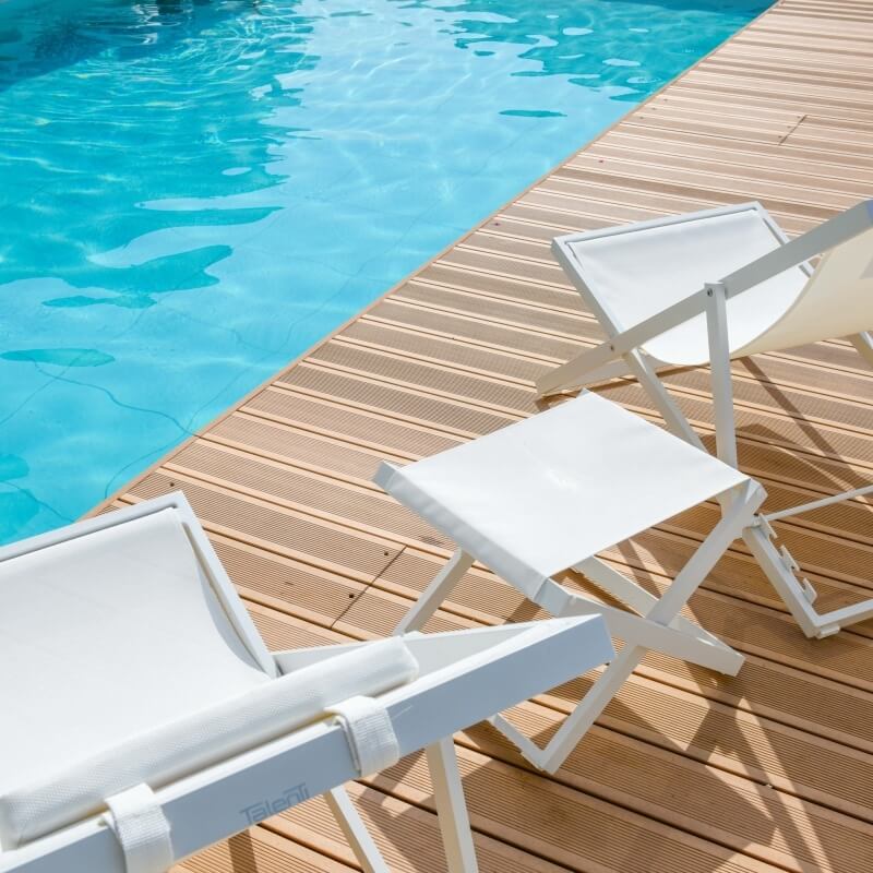 Scène paisible au bord de la piscine avec trois chaises longues blanches sur une terrasse en bois.