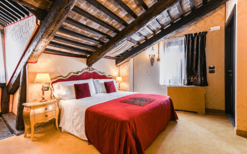 Elegantes Schlafzimmer mit hohen Decken, Holzbohlen, orangefarbenen Wänden, großem Bett und weißen Vorhängen.