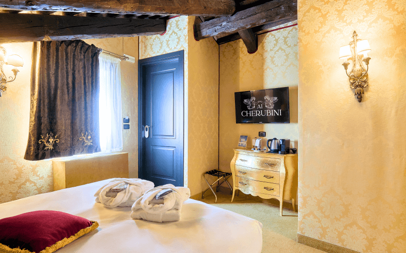 Luxuriöses Hotelzimmer mit großem Bett, Kommode, Fenster, goldfarbenen Wänden und einem einladenden Ambiente.