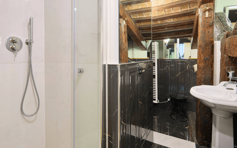Modernes Badezimmer mit Dusche, Waschbecken, Holzdecke und schwarzem Marmorboden mit goldenen Adern.