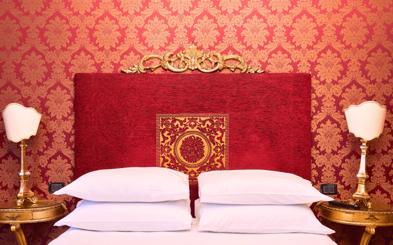 Luxuriöses Schlafzimmer mit rotem und goldfarbenem Farbschema, rotem Kopfteil, weißen Bettwäsche und goldenen Nachttischen.