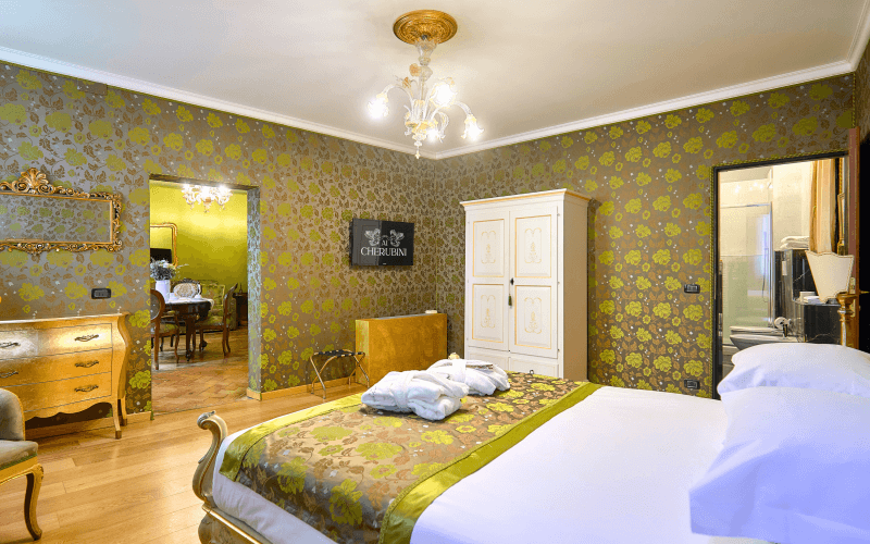 Gemütliches Schlafzimmer mit floralem Dekor, Bett mit weißer Bettdecke, Kommode, Stuhl und Kronleuchter.