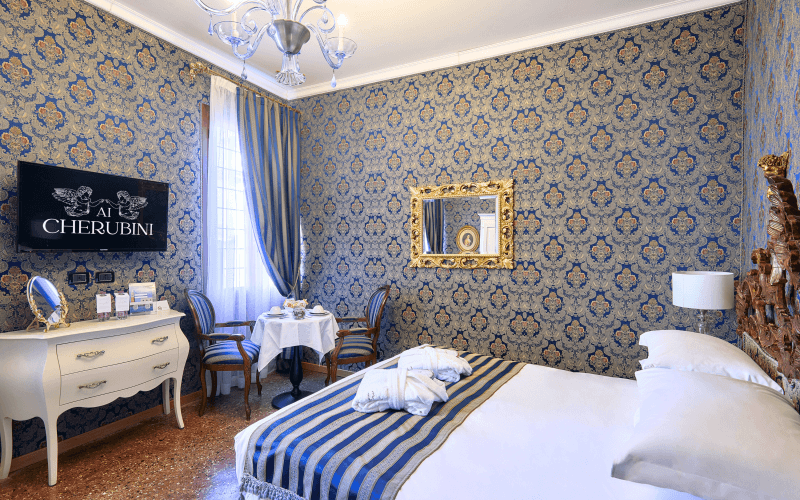 Luxuriöses Hotelzimmer mit elegantem Dekor, großem Bett, TV, Dresser, Tisch mit feinem Geschirr und goldgerahmtem Spiegel.