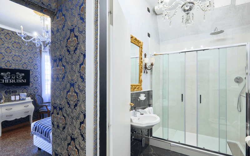 Elegantes Badezimmer mit goldenen Akzenten, Glasdusche, weißem Waschbecken und blauer, goldener Blumentapete.