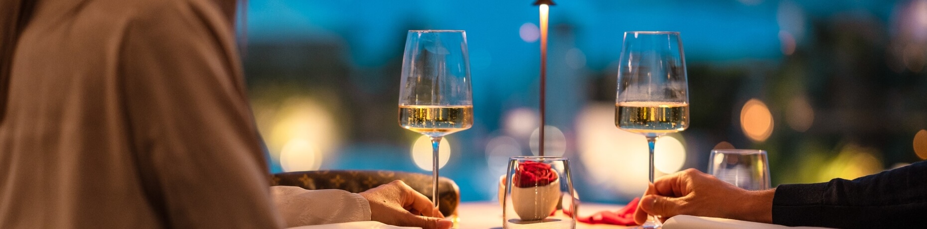 Cena romantica all'aperto con due persone formali, vino bianco e petali di rosa su un tavolo elegantemente apparecchiato.