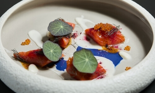 Salmone affettato con uova di pesce, salse e guarnizioni verdi.