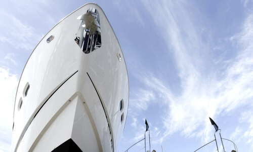 Yacht bianco con ancore sotto un cielo blu e nuvole.