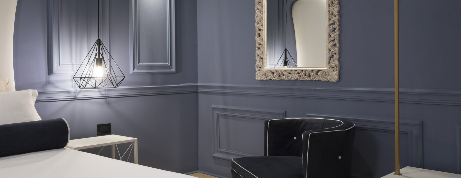 Camera d'hotel con letto, sedia nera e lampada pendente.