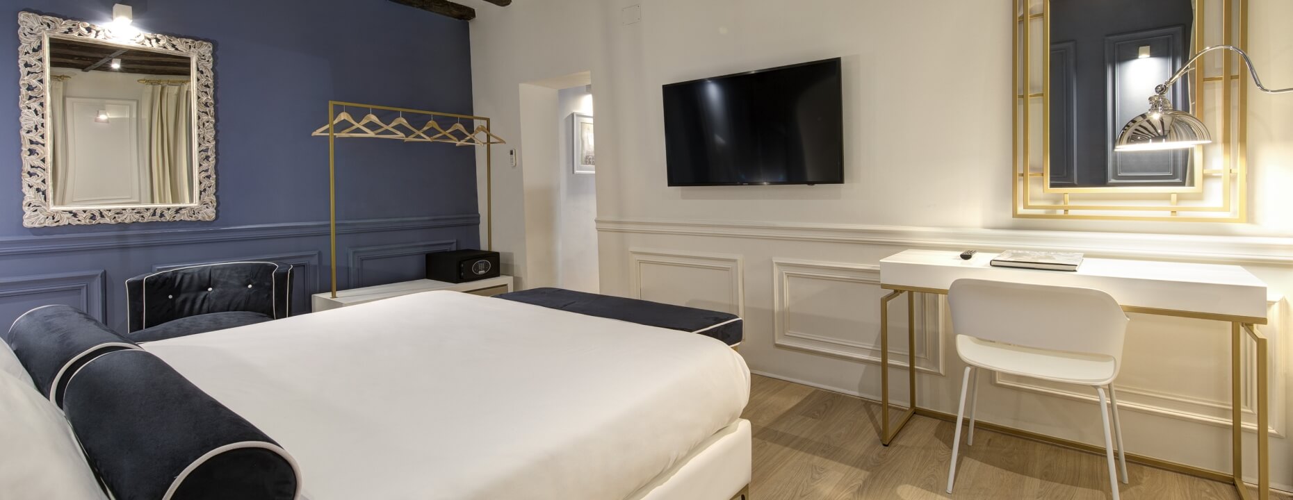 Camera d'hotel con letto bianco, mobili blu e specchi dorati.