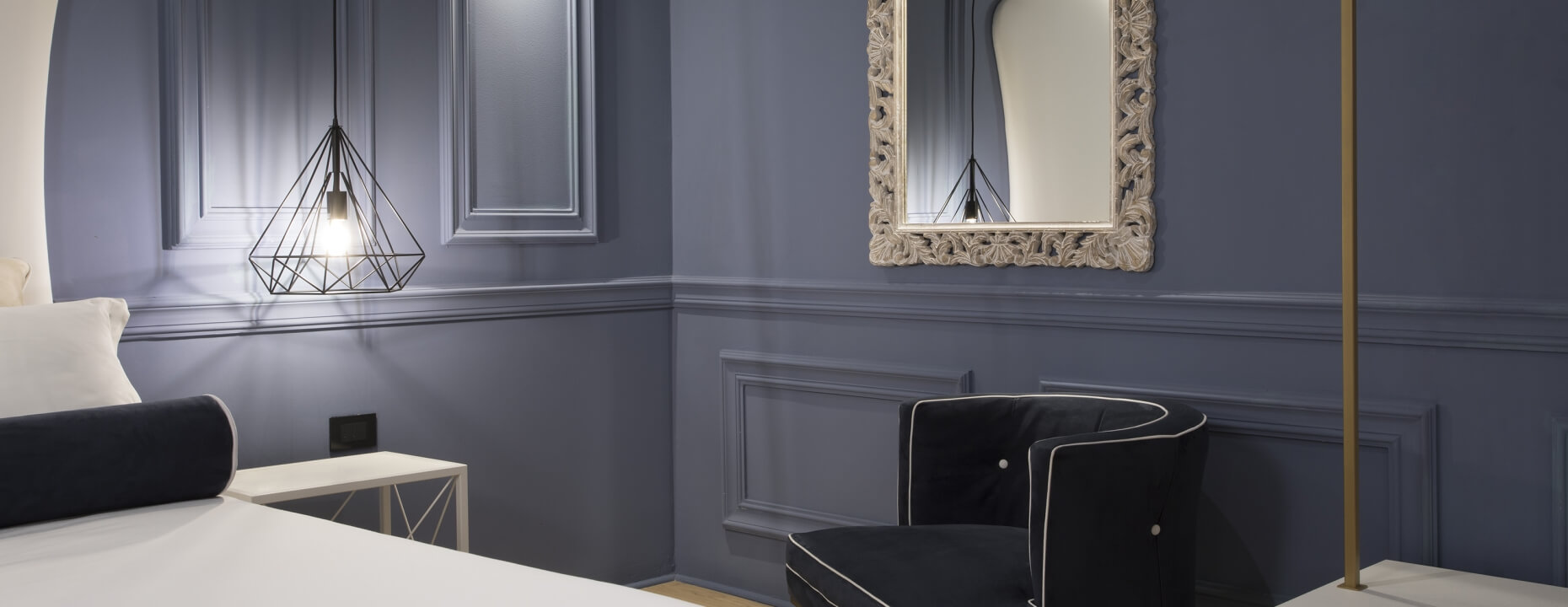 Camera con letto bianco, sedia, specchio decorativo e lampada.