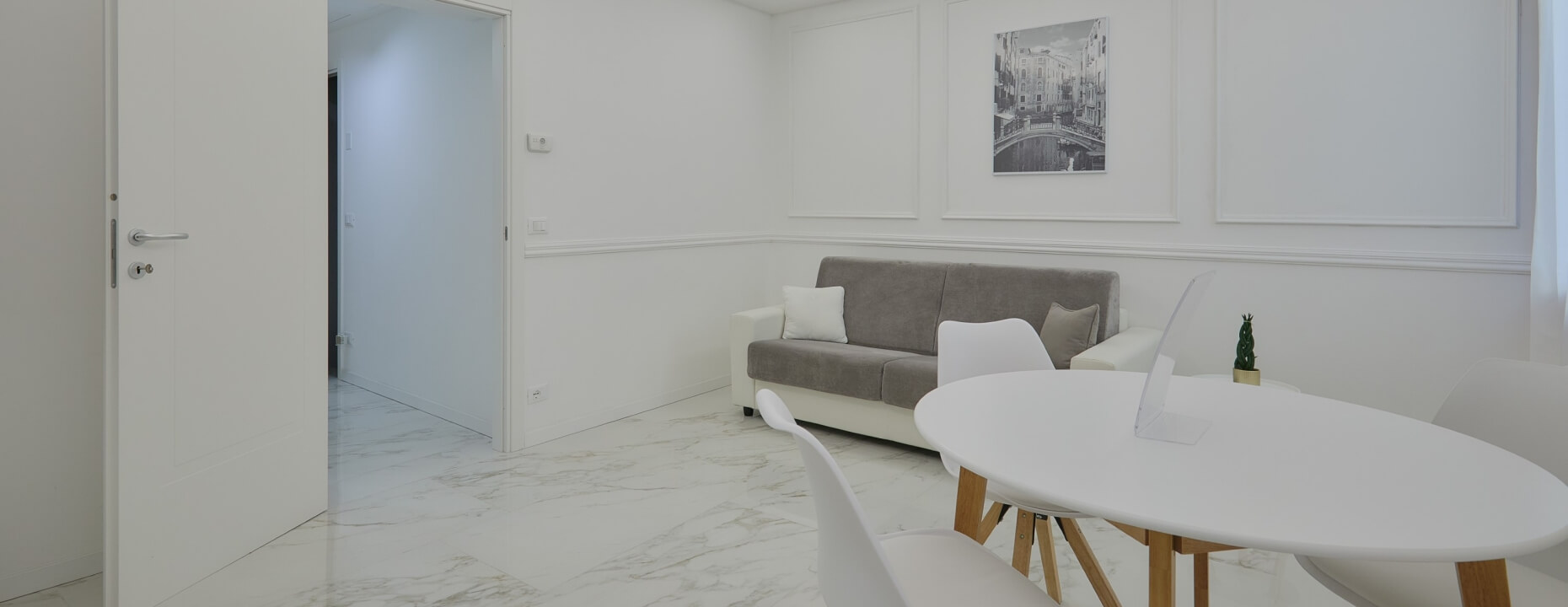 Soggiorno moderno con divano grigio, tavolo bianco e opere d'arte.