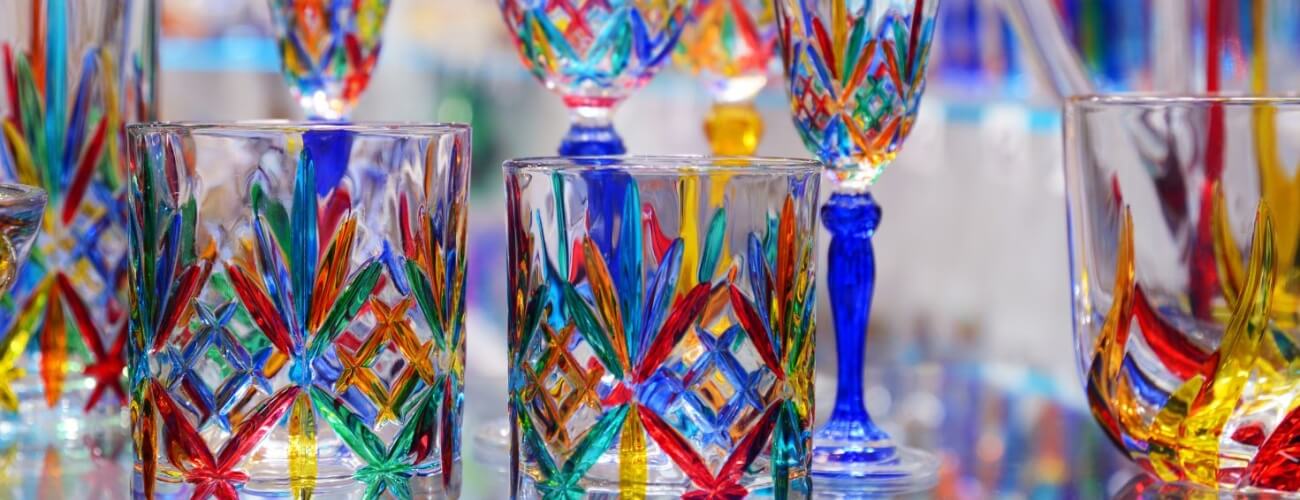Collezione di bicchieri in vetro con motivi colorati e design sfaccettato.