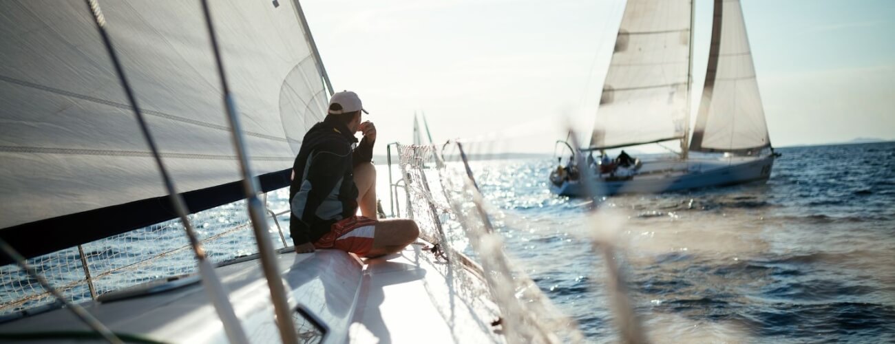 Vela su acqua, persona in giacca e cappello sul ponte.